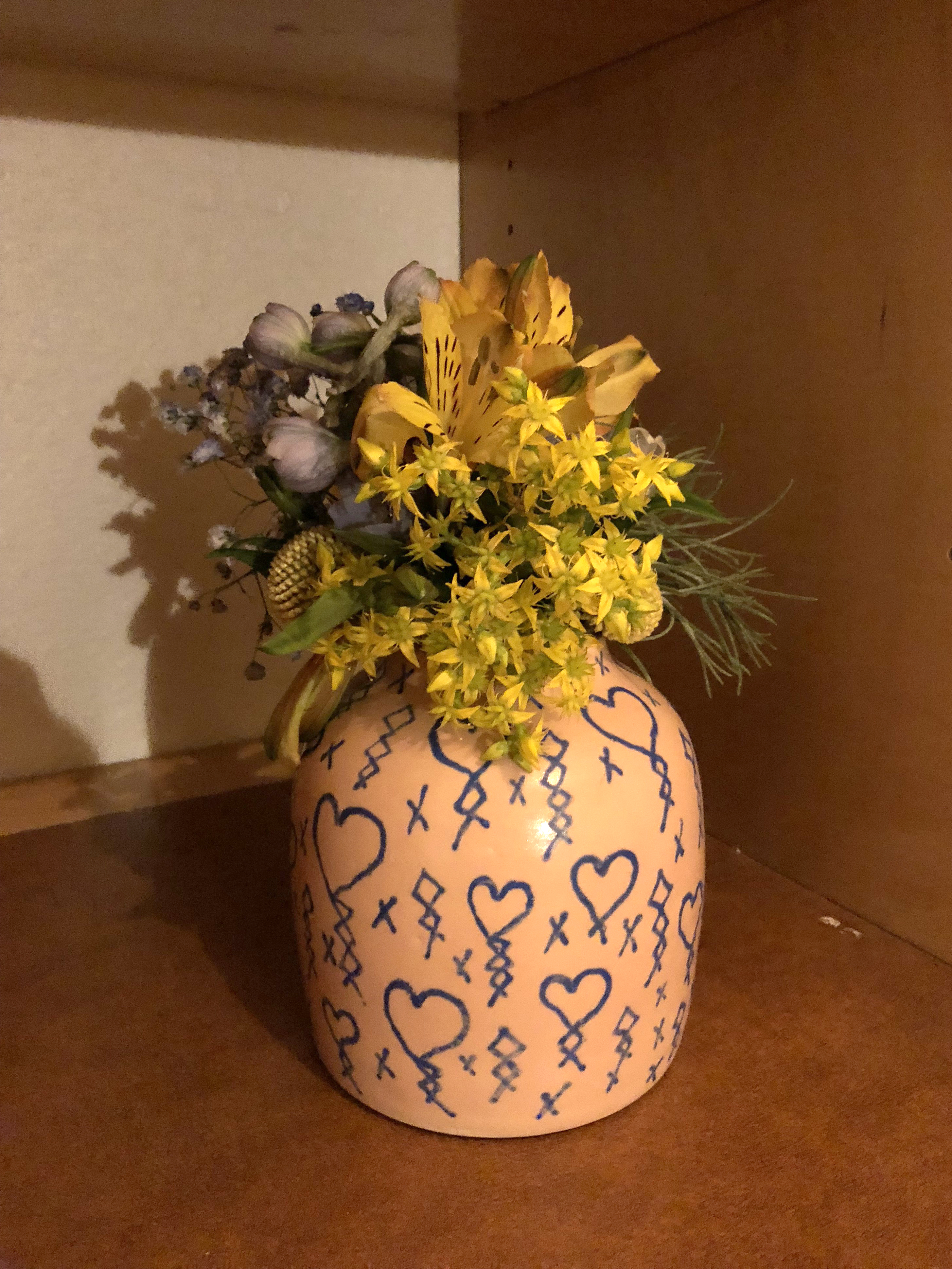 Yellow ceramic vase with drawings on it holding colorful flowers